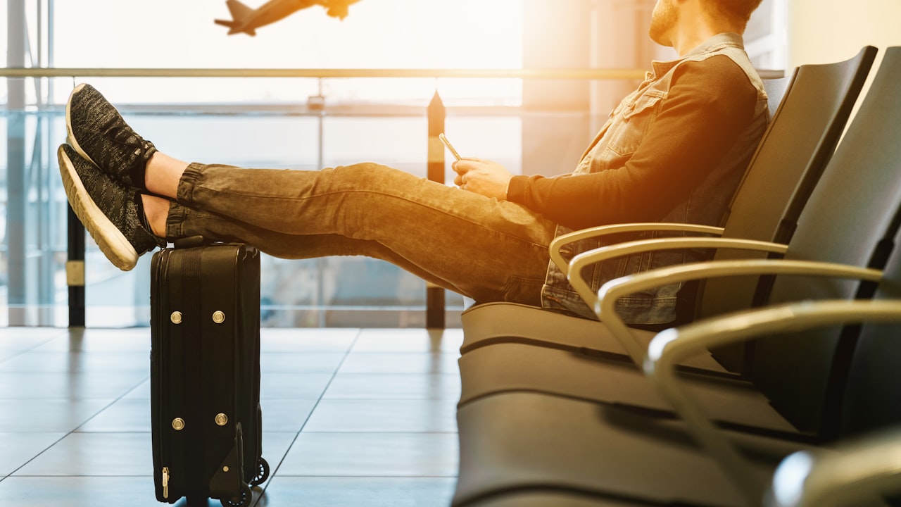 man sitting on gang chair with feet on luggage looking at airplane