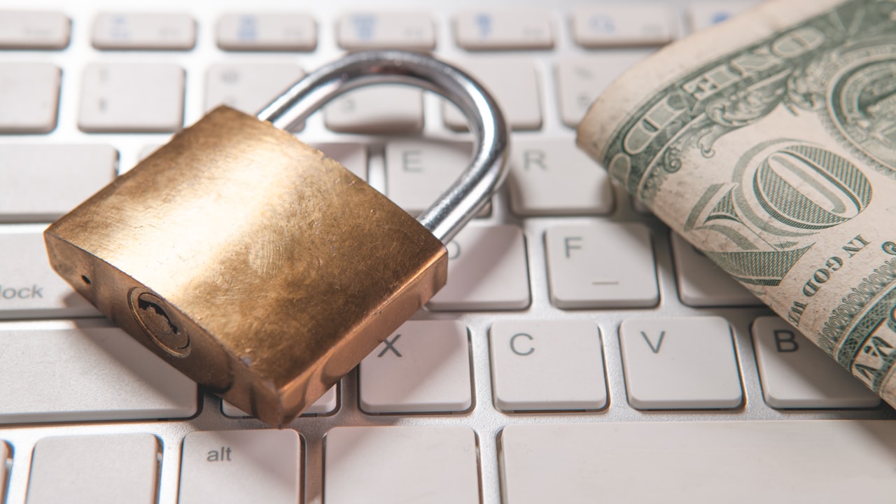 A padlock and dollar bills rest on a computer keyboard.