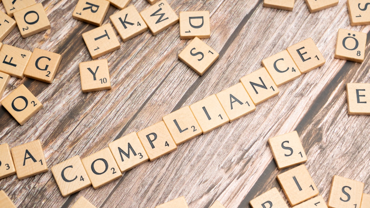 The word compliance spelled out with wooden letter tiles on a rustic table