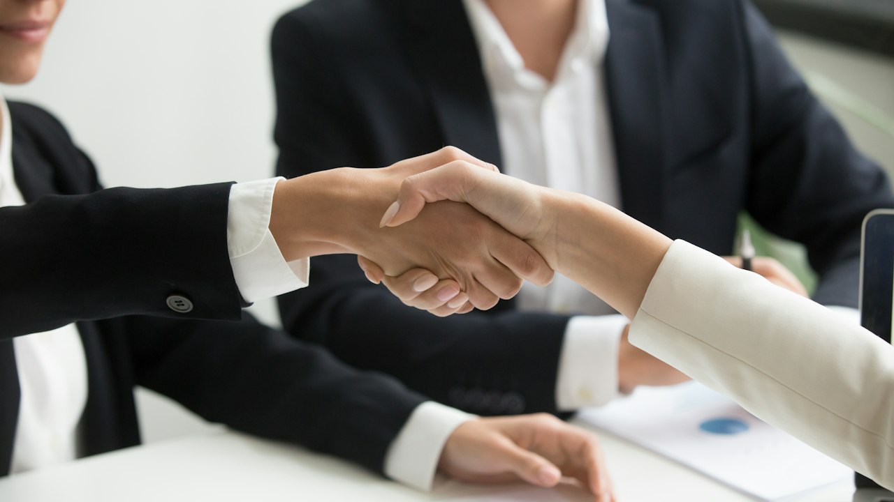 two people shaking hands in front of a laptop